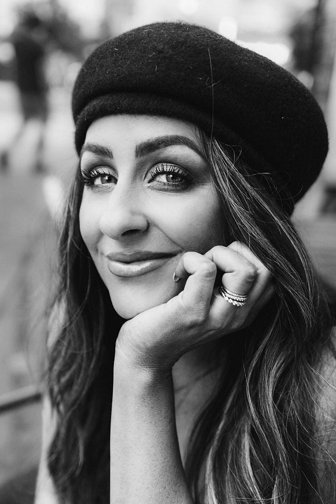Black and white portrait of Cate smiling in a beret, resting her chin on her hand
