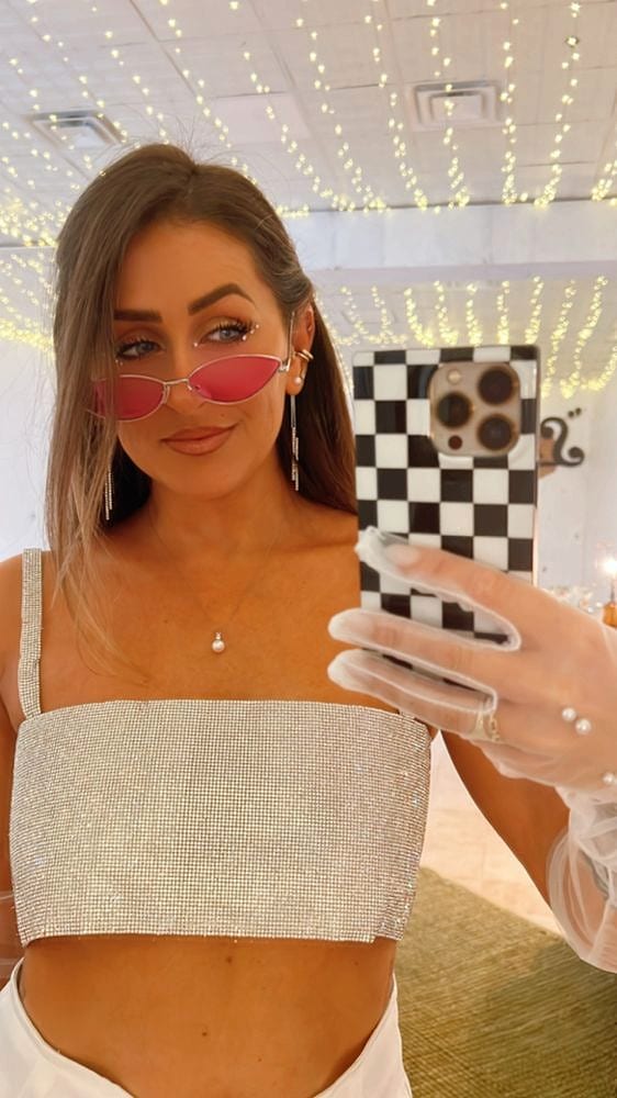 Mirror selfie of Cate in sunglasses and a sparkly top with string lights behind